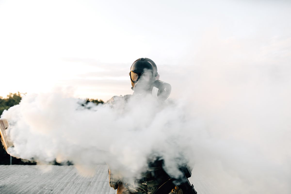 A soldier in a gas mask with a gas cylinder in front of him.