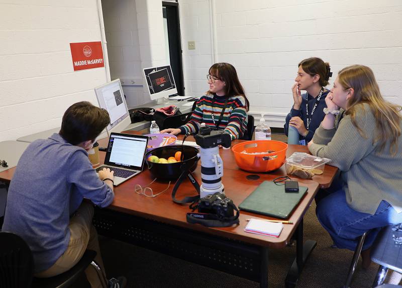 Photo coach Maddie McGarvey reviews photos taken by student Taylor Coester at a city candidates forum in Winchester Wednesday night. From left are Madison Thorn, photography participant; McGarvey; Coester; and Arden Barnes, picture editor.
