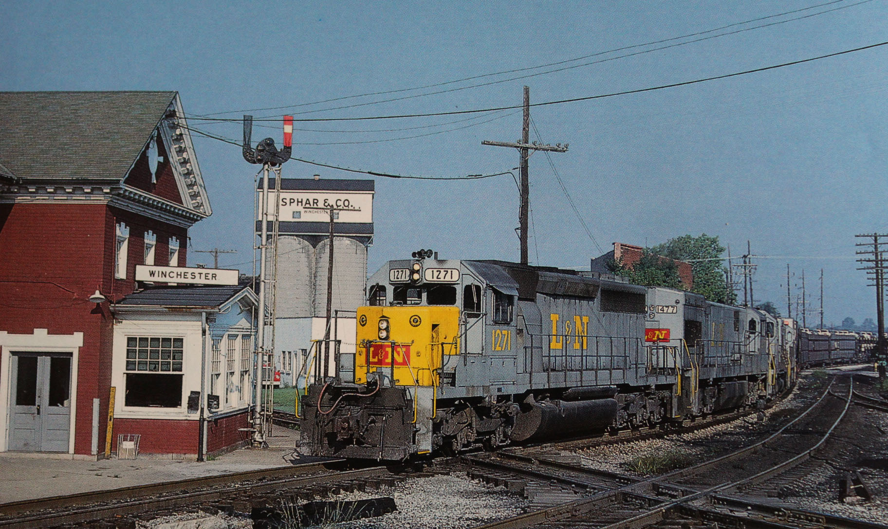 This southbound freight is approaching the L&N-C&O passenger station in Winchester in the summer of 1978. No. 1271 heads the train followed by three additional engines pulling a long string of flat cars carrying racks of new cars and trucks. (Tom DeWinter photo)