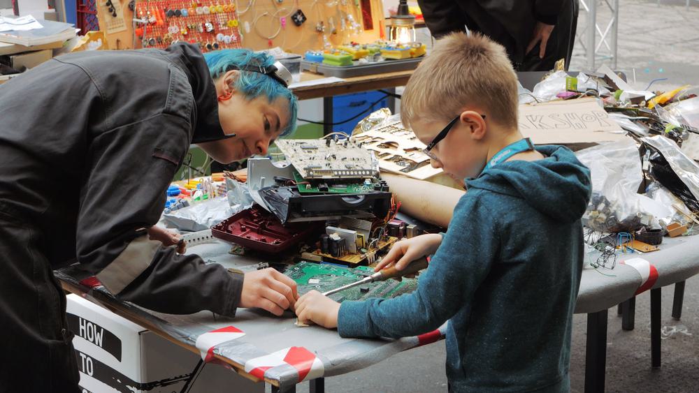 A young boy disassembles a computer motherboard at a public makerspace.
