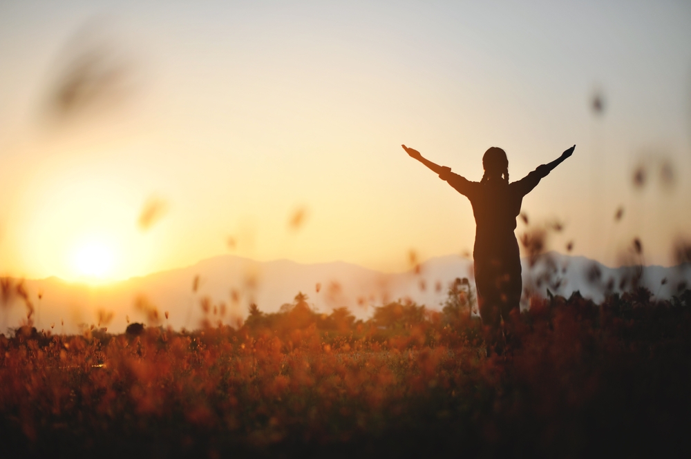 An image representing the concept of hope. A human embracing the sunrise with outstretched arms.